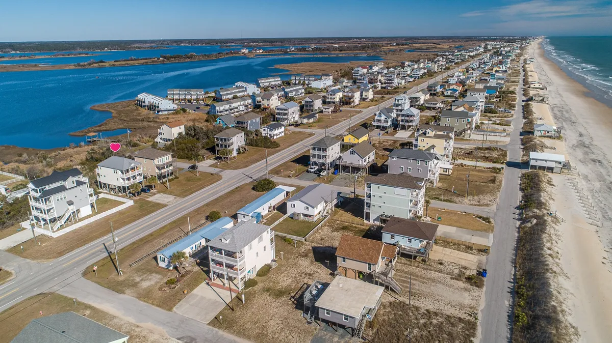 A broad exterior shot capturing beachfront homes, a coastal road, tranquil waterways, and the vast ocean beyond. The setting is inviting for beach walks, exploration, and enjoying the outdoors—activities perfect for pet owners and their dogs.