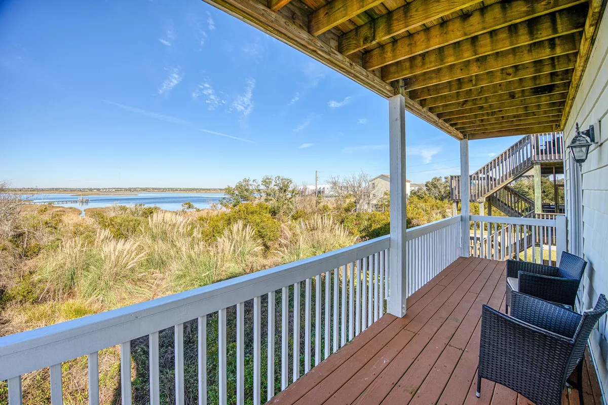 A peaceful view of the water from a deck outfitted with comfortable furniture and surrounded by lush greenery. The scene suggests a quiet spot for relaxing, reading, or simply taking in the view with a pet at your side.