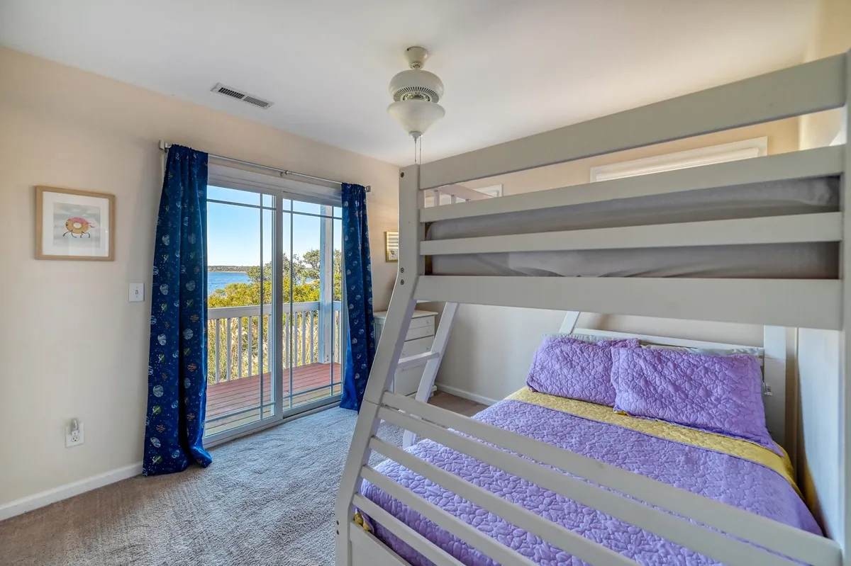 A cheerful bedroom featuring a bunk bed with colorful bedding and a sliding glass door that opens to a balcony, allowing for outside views and fresh air. The setup is perfect for kids or a playful sleepover environment.