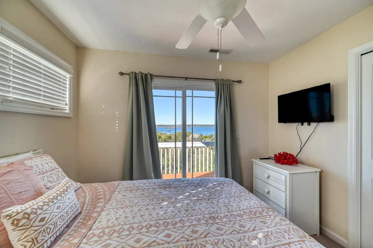 A tranquil king or queen bedroom with patterned bedding, a wall-mounted TV, dresser, and a scenic view through balcony doors. The space feels serene and provides a clear connection to the outdoor views, perfect for morning coffee or sunset relaxation.
