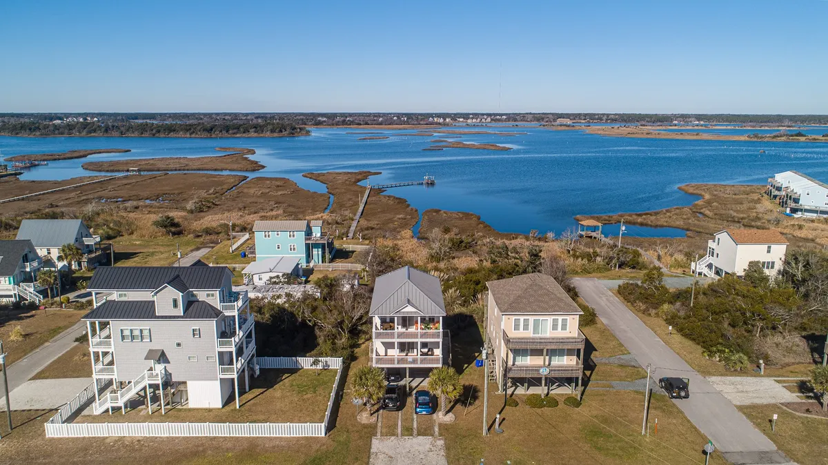 A serene waterfront view featuring a lush marshland, colorful houses, and tranquil water under a vivid sky. The landscape emphasizes the proximity to both the Intracoastal Waterway and natural habitats, offering opportunities for boating, kayaking, and wildlife observation. The horizon is open and inviting, suggesting the slow pace and relaxation that waterfront living provides.