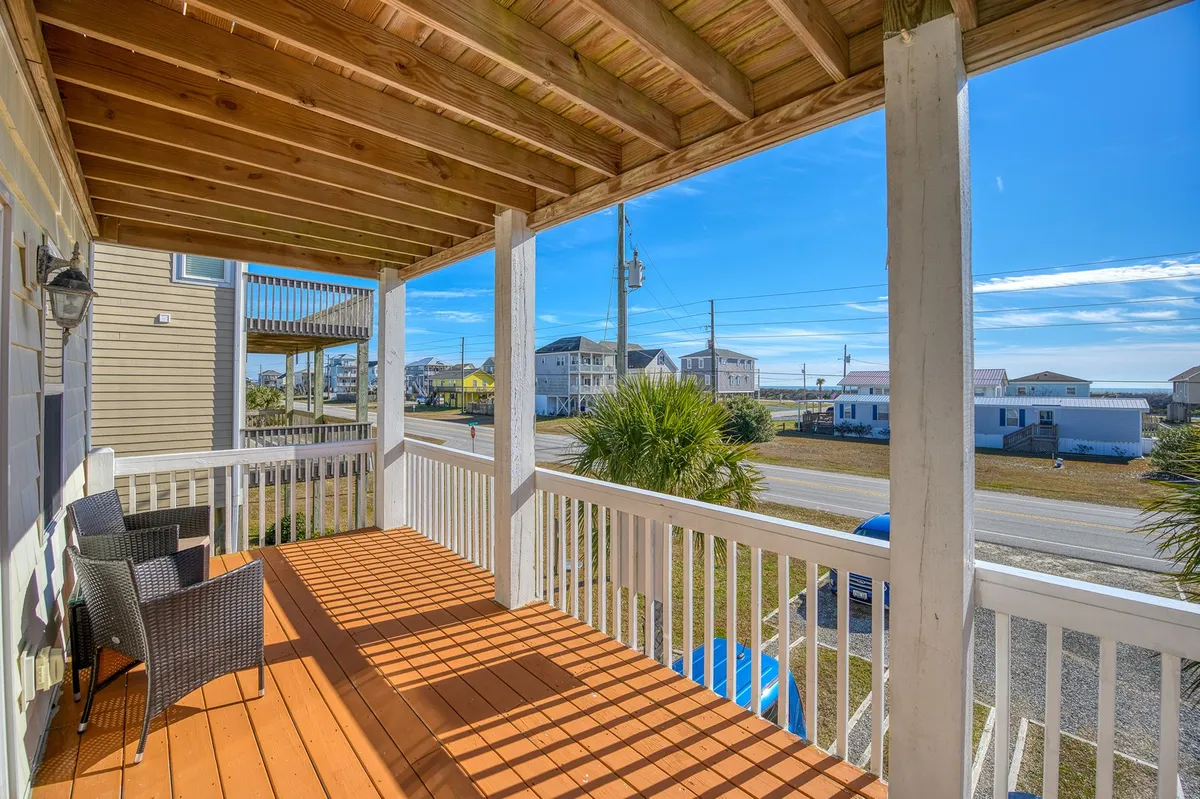 A wide wooden deck with outdoor seating overlooks the street and neighboring houses, inviting visitors to relax, enjoy the fresh air, and gather for conversation. The inviting porch is ideal for group gatherings or peaceful solo moments.