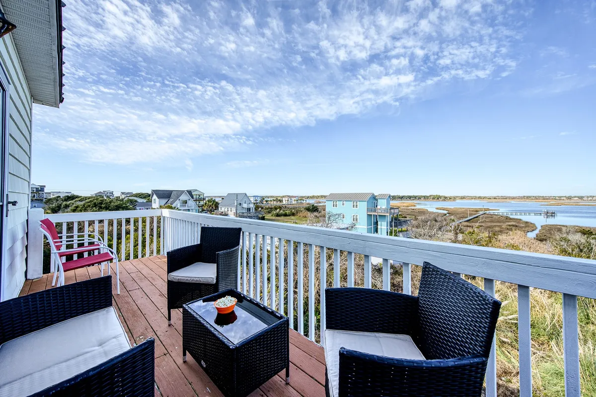 An outdoor seating area with comfortable furniture overlooks a tranquil waterway under a blue sky. The setting is perfect for unwinding, socializing, or simply soaking up water views, with the option for barbecues or stargazing at night.