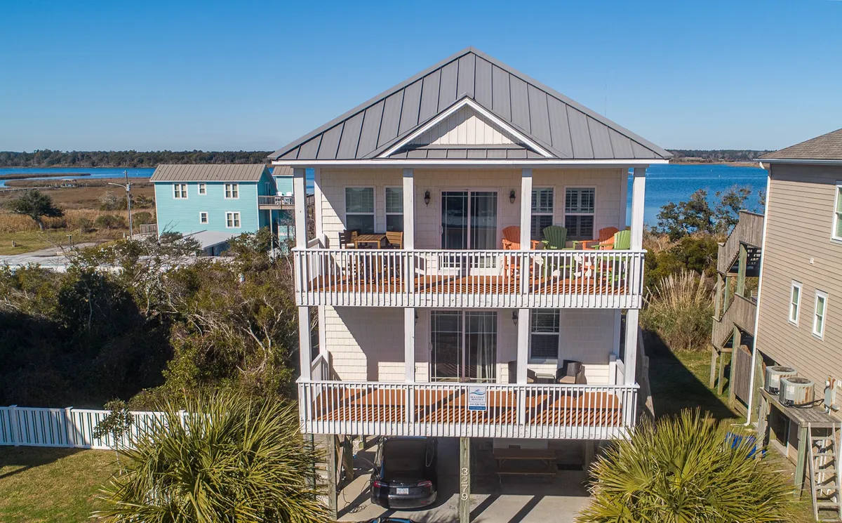 The exterior of the home with multiple balconies overlooking the water amid lush landscaping. The balconies are furnished for relaxation and offer panoramic sunrise or sunset views, ideal for unwinding after a day of adventures.