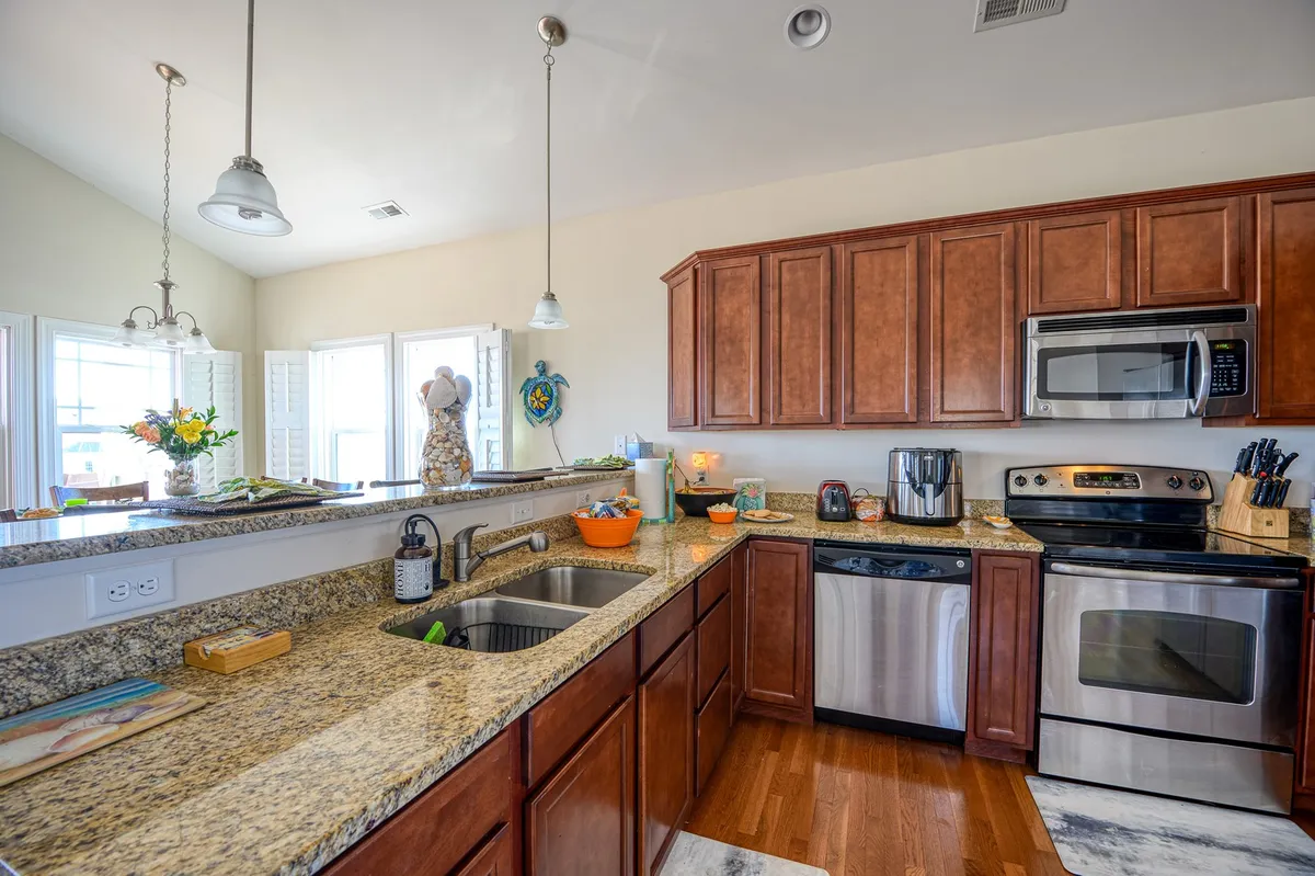 A stylish kitchen with granite countertops, wooden cabinets, stainless steel appliances, and a central island. The space is warm and welcoming, ideal for cooking, entertaining, or preparing snacks for the family. The kitchen's design and finishes mirror the upscale, fully equipped features mentioned in the narrative.