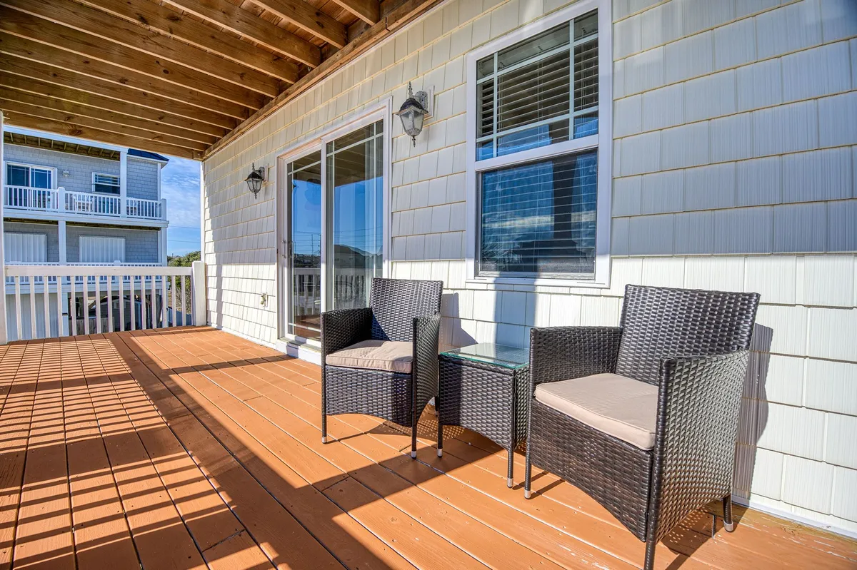 A serene wooden deck featuring outdoor seating and a glass top table, set against a backdrop of water views and open sky. The environment feels tranquil and inviting, perfect for relaxing or socializing while enjoying the natural surroundings.
